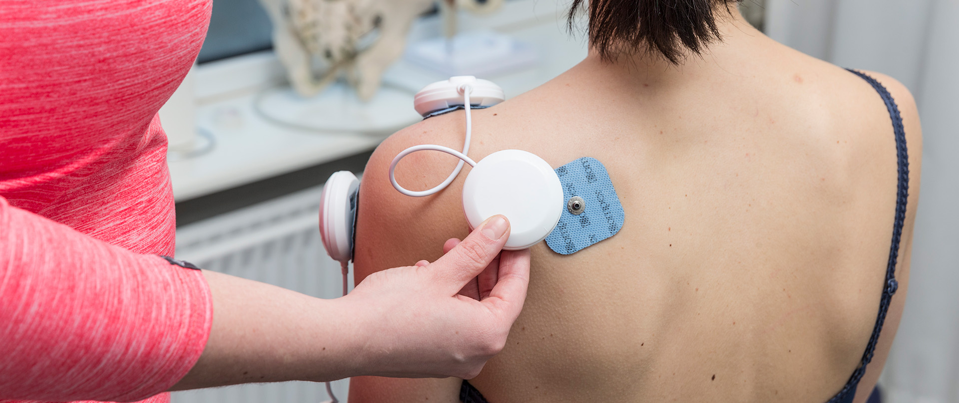 Fysioterapeut fra Fysioterapeuterne Esbjerg behandler klient ryg med Nmes - Neuromuskulær Elektrisk Stimulation mens klienten sidder op