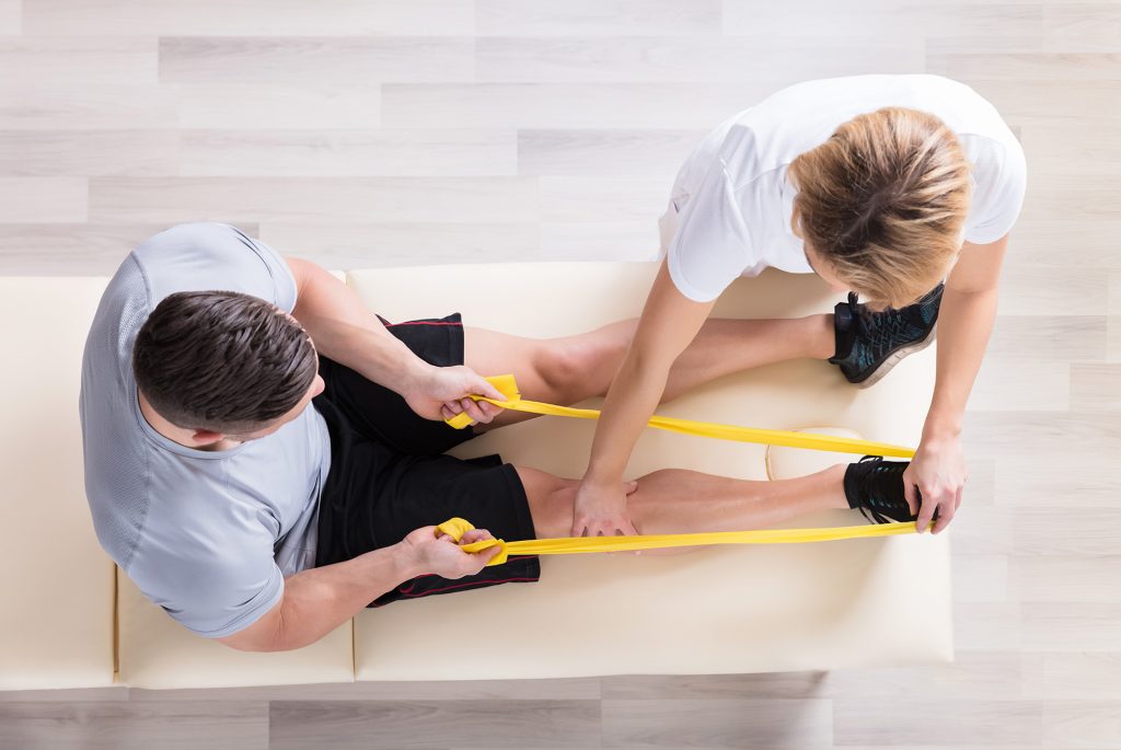 Fysioterapeut instruerer klient siddende op en briks med hjemmetræningsteknikker ved brug af en elastik